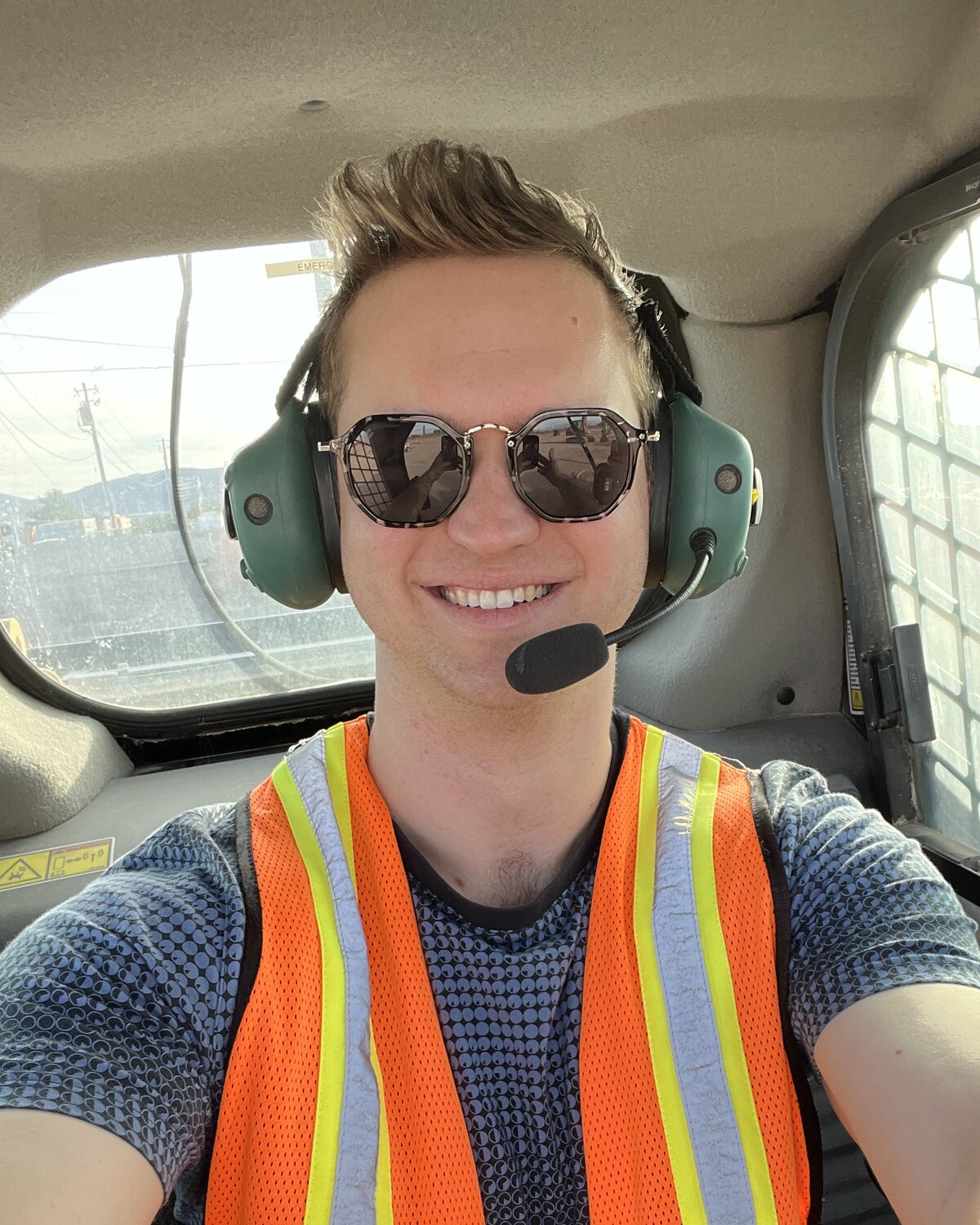Spencer Adams-Rand wearing a headset and safety vest in the cab of yard equipment at a terminal.